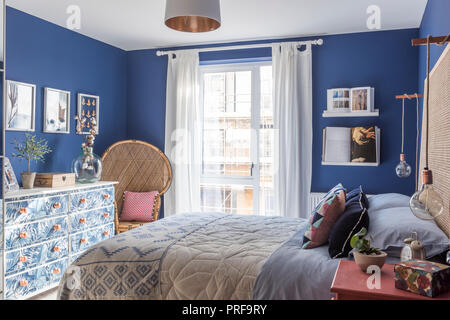 Korbstuhl und Blatt gemusterten Kommode im blauen Schlafzimmer von London Stockfoto