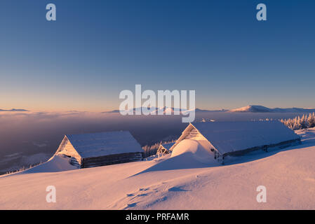 Winterlandschaft. Holzhäuser im Schnee. Tierheim Hirten auf einem Hügel. Sonniger Morgen in die Berge. Karpaten, Ukraine, Europa Stockfoto