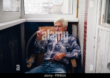 Porträt einer grauhaariger Mann 60 Jahre alt. Ein Mann sitzt in einem Sessel und raucht eine Zigarette Stockfoto