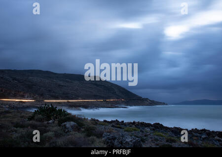 Lange Belichtung geschossen am Abend Zeit, mit Wellen brechen die Küste und Auto leuchtet eine gelbe Linie. Stockfoto