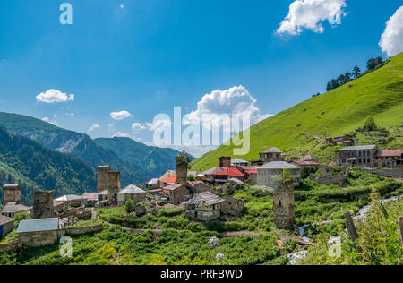 Wunderbare Aussicht auf Dorf in den Bergen gegen den blauen Himmel in der Region Swanetien, Georgia. Traditionelle alte Svan Türme auf einem grünen Hügel an einem sonnigen Tag Stockfoto