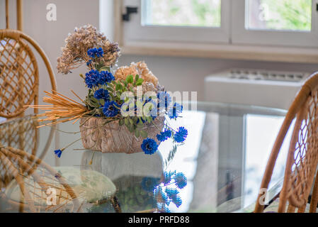 Speisesaal mit großen Glastisch und Dekorationen rund um den Ort. Getrocknete Blumen, Korbstühlen, Ton. Gemütliche Atmosphäre zu Hause. Konzept der Stockfoto