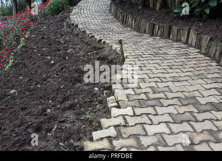 Kurve brick Bürgersteig entlang der unvollendete Blume Garten auf dem Hügel. Stockfoto