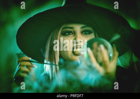 Close-up auf eine Hexe mit schrecklich Gesicht und Magic Ball in der Hand in der nebligen Umgebung sendet das Böse. Stockfoto