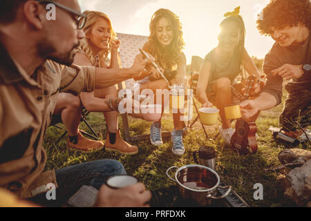 Glückliche junge Freunde genießen Sie einen sonnigen Tag in der Natur. Sie kochen Kaffee, lachen und reden gerne zusammen zu sein. Stockfoto