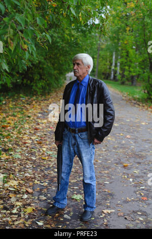 Grauhaariger Mann mit einem Regenschirm in der Hand auf der Straße. Ein Mann ist 60 Jahre alt. Stockfoto