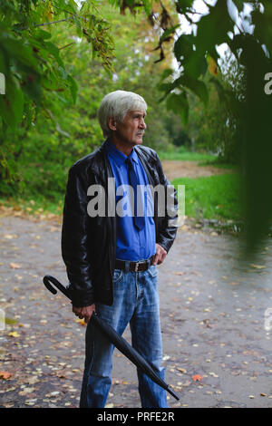 Grauhaariger Mann mit einem Regenschirm in der Hand auf der Straße. Ein Mann ist 60 Jahre alt. Stockfoto