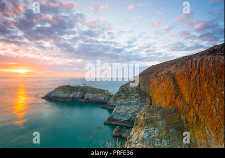 Abend Landschaft schoss der untergehenden Sonne mit Blick aufs Meer in Richtung South Stack Lighthouse, Anglesey, Nordwales. Glühende Felsen am späten Abend licht. Stockfoto