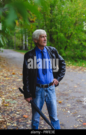 Grauhaariger Mann mit einem Regenschirm in der Hand auf der Straße. Ein Mann ist 60 Jahre alt. Stockfoto