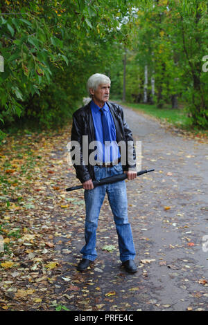 Grauhaariger Mann mit einem Regenschirm in der Hand auf der Straße. Ein Mann ist 60 Jahre alt. Stockfoto