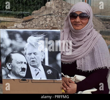 London, GB, 13. Juli 2018. 100.000 Menschen protestieren gegen den Besuch des US-Präsidenten Donald Trump. Die Demonstranten versammeln sich auf dem Trafalgar Square. Eine Frau trägt ein Kopftuch und einer Sonnenbrille sitzt gelassen mit einem Photoshopped schwarz-weiß Bild von Donald Trump mit Adolf Hitler. Stockfoto