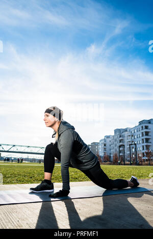 Entschlossene junge Frau ihr Bein stretching Während kniend auf einer Matte Stockfoto