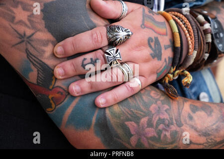 Stark und der Hand des bunten tattooed Lady ruhen auf ihren Arm, während das tragen mehrere große silberne Ringe und Riegel style Armbänder. Stockfoto