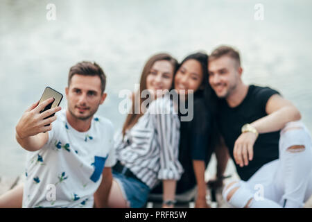 Freunde selfie sitzen auf Pier mit See Hintergrund beim Picknick ausruhen. Freundschaft und Spaß Konzept Stockfoto