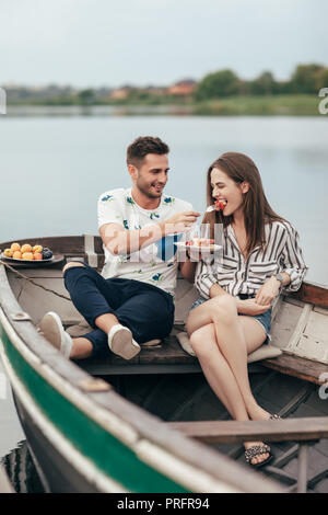 Romantisches date. Mann seine Freundin Kuchen füttern. Gerne attraktive Paare sitzen auf dem Boot in den Fluss Beziehung Konzept Stockfoto