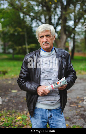 Ein Porträt von einem grauen Mann ist 60 Jahre alt. Er hält eine Zeitung in den Händen. Der Mann hat schlechtes Sehvermögen, er eine Brille trägt Stockfoto