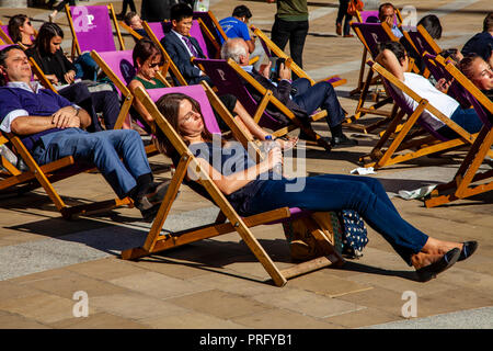 Menschen sitzen in Liegestühlen Im Herbst Sonnenschein, Paternoster Square, London, UK Stockfoto
