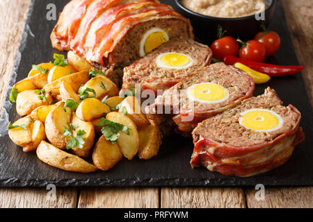 Köstliche Speck umwickelt Meat Loaf mit Ei mit Kartoffelecken und Sauce close-up auf einer Schiefertafel Platte auf den Tisch serviert. Stockfoto