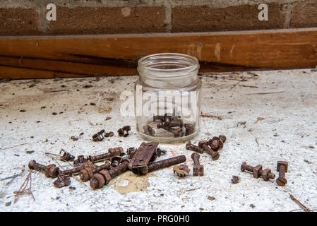 Jar der rostigen Schrauben, Muttern, Scharniere und Scheiben auf einem Workshop Bank. Stockfoto