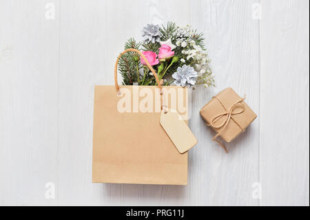 Weihnachten mockup Shopping Konzept. Kraft Paket mit Holz- tag und xmas Dekor Tannenzweigen, Rosen, Kegel mit Platz für Ihren Text. Stockfoto