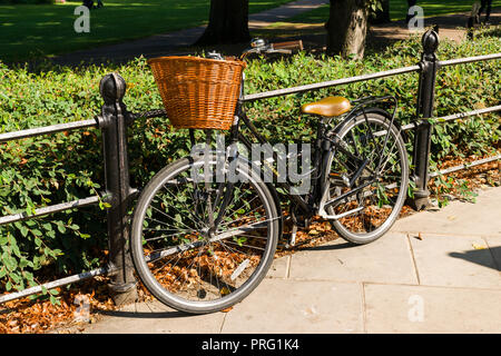 Einen altmodischen schwarzen Damen Fahrrad mit Weidenkorb auf der Vorderseite Fastenzeit gegen Geländer an einem sonnigen Tag, Cambridge, Großbritannien Stockfoto