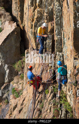 Portrait einfangen, drei Männer genießen Herausforderung der Extreme Sport: Abseilen und Klettern auf der Felswand an der South Stack Klippen, Anglesey, UK. Stockfoto