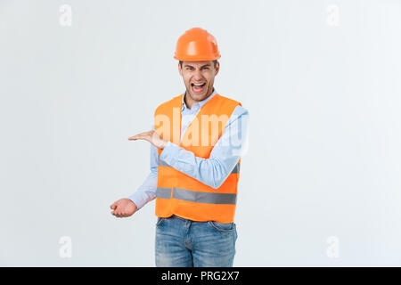 Happy Bart Ingenieur die Hand auf die Seite legen und etwas erklären, Guy tragen caro Shirt und Jeans mit gelber Weste und Helm, orange auf weißem Hintergrund Stockfoto