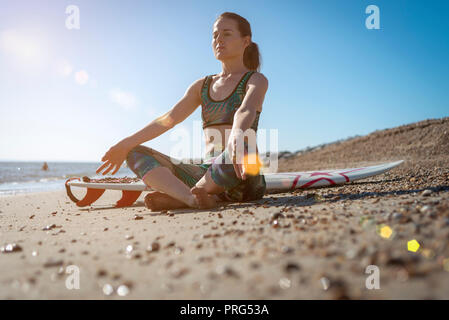 Weibliche Surfer am Strand zu sitzen meditieren Yoga vor dem Surfen., warten auf den Wellen. Stockfoto
