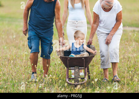 Familie drücken ihre kleinen Kinder und Enkel in einer Schubkarre Stockfoto