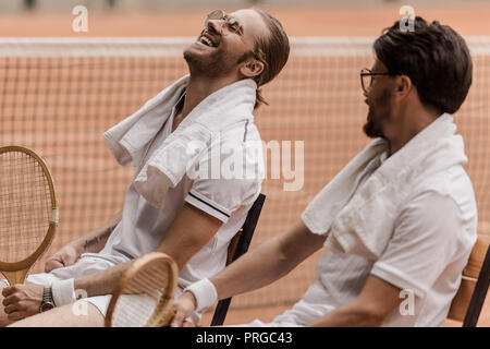 Lächelnd im Retrostil tennis Spieler sitzen auf Stühlen mit Handtüchern und Schläger am Tennisplatz Stockfoto