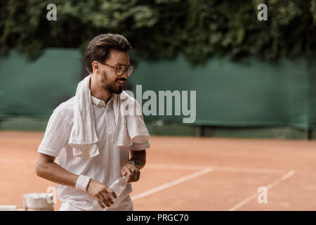 Lächelnd stattlichen Tennis Spieler, Flasche Wasser am Tennisplatz Stockfoto