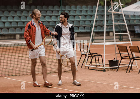 Lächelnd stattlichen Tennisspieler wandern und sich an der Suche am Hof Stockfoto