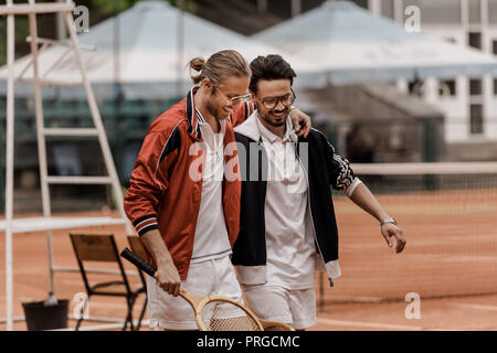 Lächelnd im Retrostil tennis Spieler gehen mit Schläger und umarmen am Tennisplatz Stockfoto