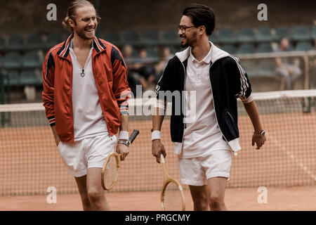 Lächelnd im Retrostil Tennisspieler wandern und an jedem anderen, Tennisplatz Stockfoto