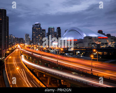 Toronto's Rogers Centre Kuppel von Gardiner Expressway mit leichte Züge, die Bewegung des Verkehrs auf Straßen mit Gebäuden im Hintergrund Stockfoto