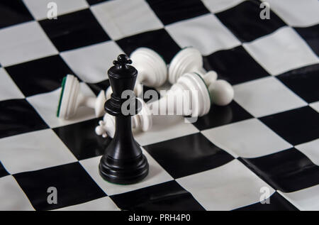 Schwarz chess König stehend auf Schachbrett, weiße König gefallen mit Bauern. Strategie, Finanzen, Business Konzept. Stockfoto