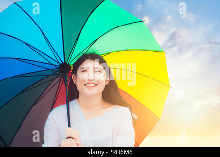 Cute Asian teen glückliches Lächeln im Freien mit Regenbogen bunten Regenschirm sonnigen Tag Stockfoto
