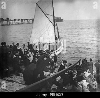 Ein spät-viktorianischen Foto, Gruppen von Menschen, einige Aussteigen aus einem kleinen Boot, und mit einem Pier im Hintergrund, einem Badeort in England. Stockfoto