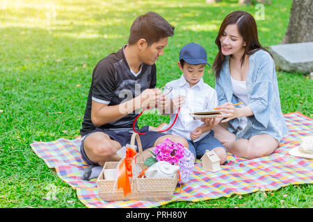 Asian teen Familie lehre Sohn Hausaufgaben beim Picknick im Freien Park Stockfoto