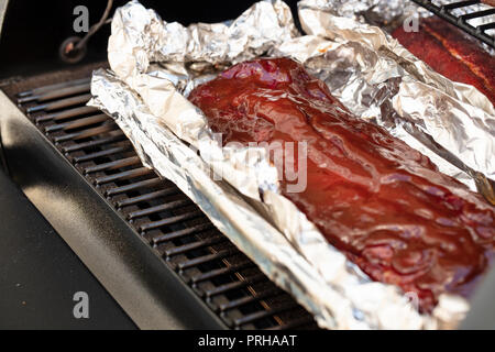 Eine Platte von Rippchen mit Barbecue Sauce auf einem Grill Tor und Aluminiumfolie Stockfoto