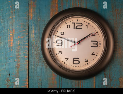 Zeit Konzept, rund, schwarz Wanduhr gegen alte Holz- blauer Tisch. Stockfoto