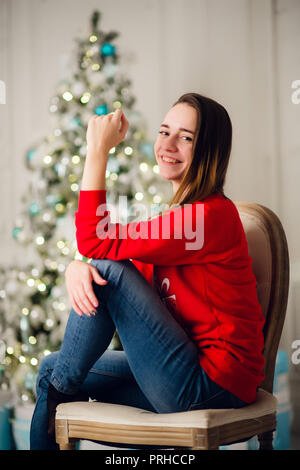 Glückliche junge Frau sitzt in der Nähe von Weihnachtsbaum. Stockfoto