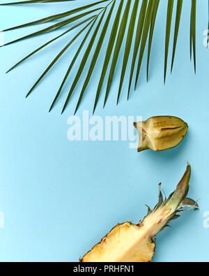 Zusammensetzung von einem Palm Leaf, Hälften von Ananas und karambolen auf einem blauen Hintergrund mit kopieren. Exotische Früchte. Flach Stockfoto