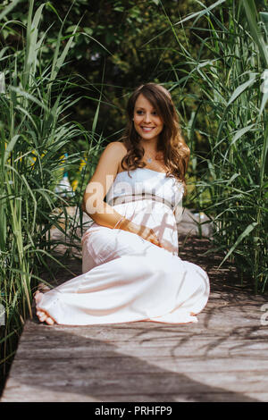 Portrait von schöne schwangere Frau sitzt auf dem Boden und lächelt Stockfoto
