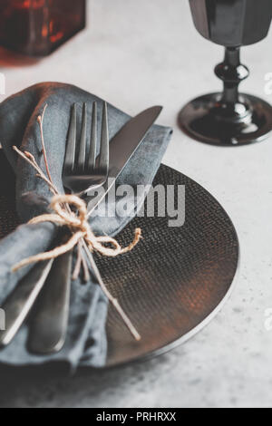 Festliche Tischdekoration in einem schwarzen Stil unter schwarzen Kerzen auf einem weißen Tisch. Mit Messer und Gabel auf einem Leinen Servietten Teller. Thanksgiving oder Halloween di Stockfoto