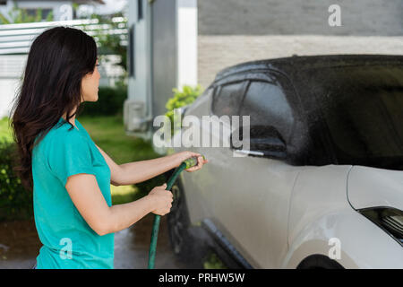 Junge Frau Wasser sprühen ihr Auto mit Wasser waschen, Stockfoto
