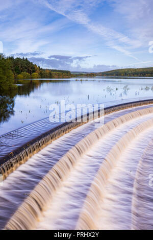 Wasser fließt über abflußkanal von ruhigen malerischen Bäumen gesäumten See, unter tief blauen Himmel - Fewston Reservoir, Washburn Tal, North Yorkshire, England, UK. Stockfoto