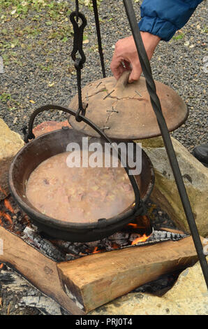 Vorbereiten der Gulasch auf offenem Feuer in einem Wasserkocher, Hebezeuge Ton Abdeckung, und prüfen Sie, ob ein Staat von Speise Stockfoto