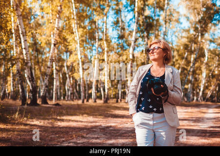 Frau mittleren Alters Aufnehmen von Bildern mit der Kamera im Herbst Wald. Stilvolle senior Frau Wandern und Genießen Hobby Fotografieren Stockfoto