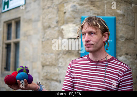 Eine Street Performer seine Balanceakt Brunnen Marktplatz. Er ist auch ein Musiker, spielt eine Gitarre und Geige. Wells, Somerset, Großbritannien Stockfoto